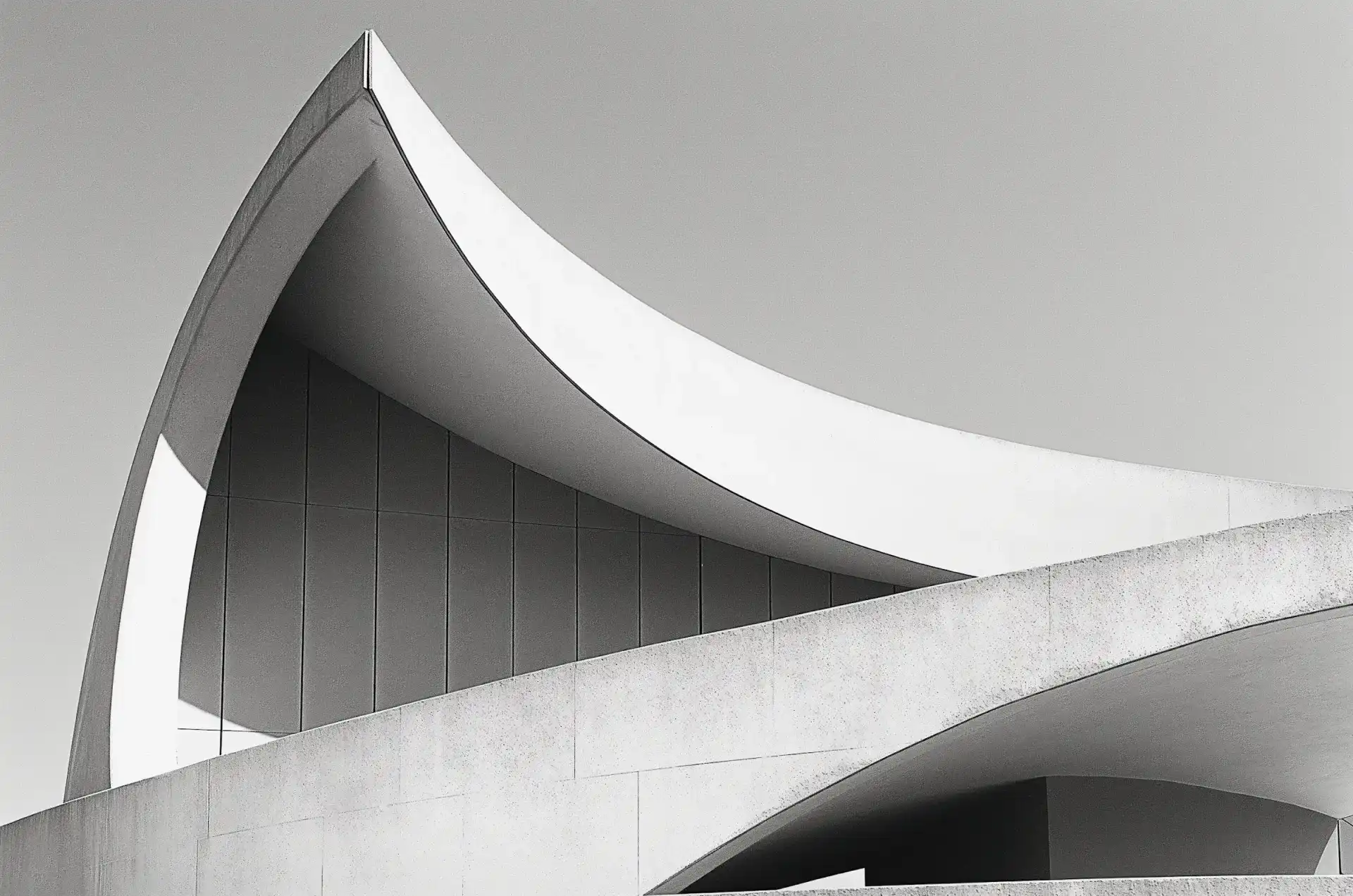 Black and white photo of a modern, curved architectural structure against a clear sky.